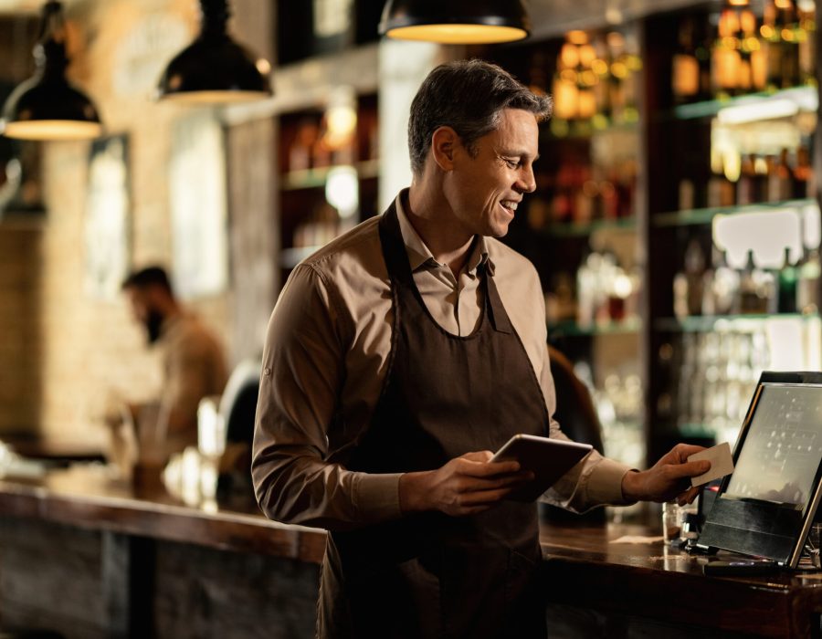 Happy barista adding an order to cash register while working in a pub.