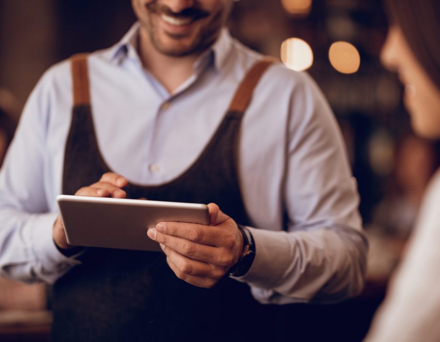 Close-up of waiter taking order on touchpad while talking to a guest in a pub.